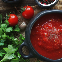 tomato soup with fresh herbs, clove, black pepper and crackers on rustic wooden background, top view.