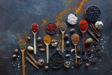Fototapeta na wymiar Various indian spices in wooden spoons and metal bowls, herbs and nuts on dark stone table. Colorful spices, top view,space for text. Healthy food background