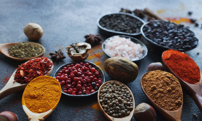 Various indian spices in wooden spoons and metal bowls, herbs and nuts on dark stone table. Colorful spices, selective focus. Healthy food background