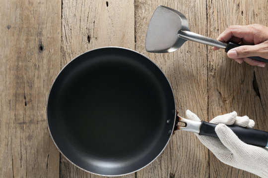hands holding cooking pan with spatula on old wooden background.