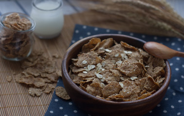 Wooden bowl of organic cornflakes and oatmeal, milk in a glass bottle, selective focus. Nutritious breakfast, raw food ingredients, healthy lifestyle