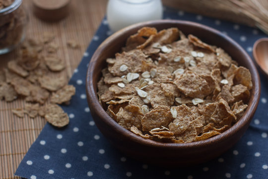 Wooden bowl of organic cornflakes and oatmeal, milk in a glass bottle, selective focus. Nutritious breakfast, raw food ingredients, healthy lifestyle