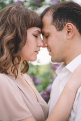 beautiful couple, the girl in beige light dress, the guy the white shirt, cuddling with their eyes closed, foreheads pressed against each other near the tree, greens, summer, lilac, close-up, nature