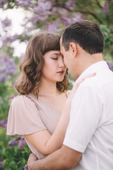 beautiful couple, the girl in beige light dress, the guy the white shirt, cuddling with their eyes closed, foreheads pressed against each other near the tree, greens, summer, lilac, close-up, nature