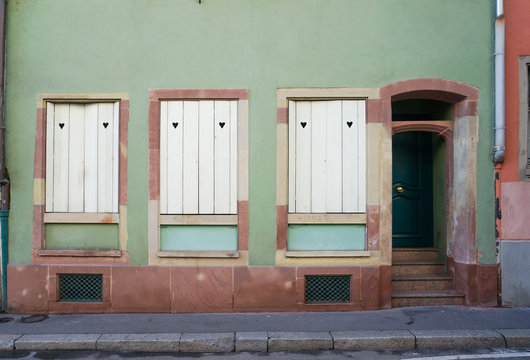 Pastel green and dark brown building with white windows and door beside the street in Colmar, France