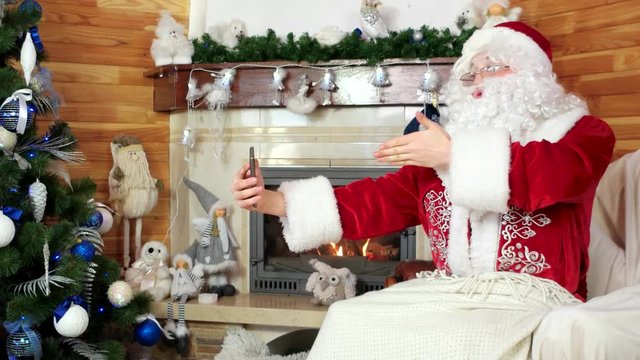 santa talking via skype, santa claus using gadget, decorated christmas tree, saint nicolas sending merry kisses by videocall, christmas preparation, room with fireplace, using digital device for volte