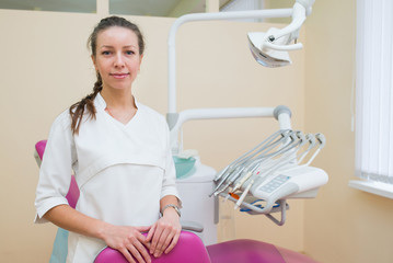 Fototapeta premium Portrait of young female dentist, standing in dental office smiling and looking at camera.