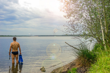 Mann mit Schwimmbrille und Flossen am See, Training für einen Triathlon