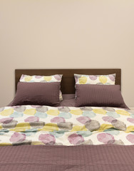 Bed with pillows and bedding sheets against beige wall