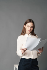 Businesswoman holds the papers in her hands and reads what is written there. Isolated on gray background.