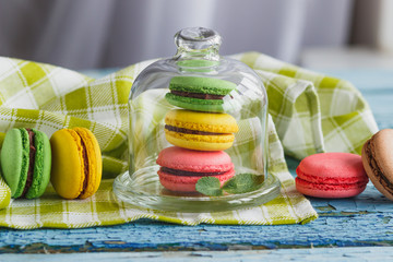 Green, pink and yellow french macarons under the glass on the wooden boards