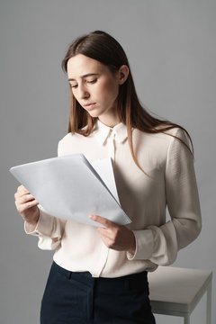 Businesswoman holds the papers in her hands and reads what is written there. Isolated on gray background.