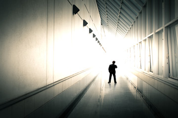 Miniature people : businessman standing in office building corridor against light