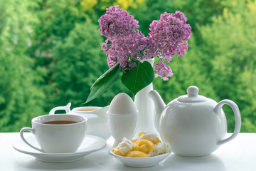 White crockery for tea on a natural green background. Teapot, Cup, creamer, stand for eggs and a...