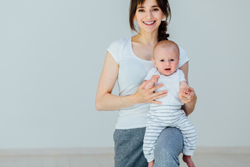 Athletic young smiling woman in sports dress doing fitness exercise with little baby boy on her knee. Mother having fun and working out with her little son.
