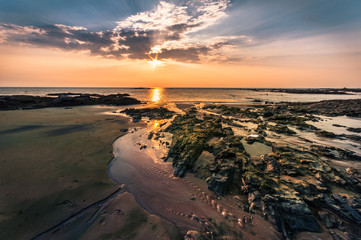 Beautiful seascape. Sunset over the sea rock and shore. A thin orange line at the horizon and the blue sky background and moss on rock foreground with the sunlight reflection on the water - wide angle