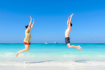 The happy Cheerful couple enjoys relaxing and jumping at white sand beach with blue sky and blue sea background.