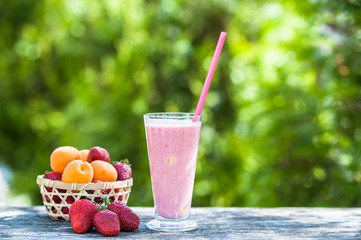 Wicker basket with strawberries and apricots, glass with strawberry smoothies, natural wood background	