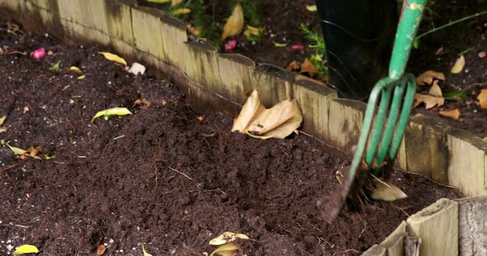 Person mixing soil with fork in garden