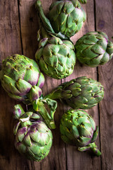 Bunch of ripe fresh colorful organic artichokes scattered on weathered wood table, rustic style,...