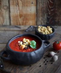 Tomato soup with croutons in a black handmade ceramic plate on wooden background, Rustic