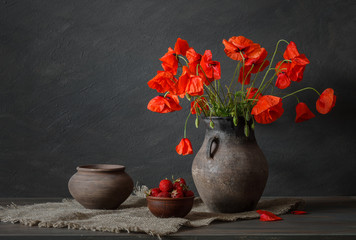 Still life in a rustic style: potteries, strawberry and a bouquet of red poppies