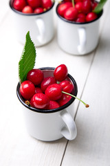 Cherry in enamel cup on white wooden background. Healthy, summer fruit. Cherries...