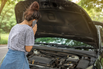Asian woman using mobile phone while looking at broken down car on street