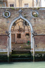 Venice, Cannaregio, Veneto, Italy. Graceful old Gothic style arched water door in a weathered brick wall  with seaweed covered steps  off a canal leading in  into a courtyard