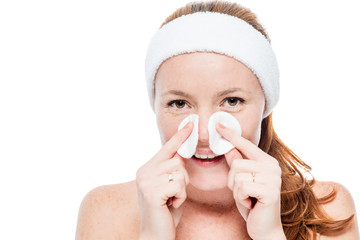 Smiling woman with freckles wiping her face with cotton pads on white background