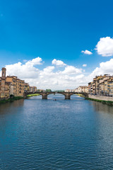 Naklejka premium Vertical composition the River Arno in Florence with puffy clouds and rowers on the water.
