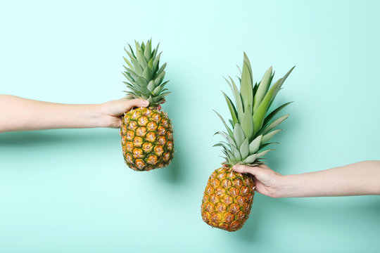Female hands holding ripe pineapples on mint background