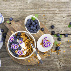 Obraz na płótnie Canvas Healthy Breakfast: homemade roasted granola with blueberries, kiwi fruit and edible flowers on wooden background. From the top view. The concept of fitness nutrition