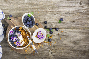 Healthy Breakfast: homemade roasted granola with blueberries, kiwi fruit and edible flowers on wooden background. From the top view. The concept of fitness nutrition