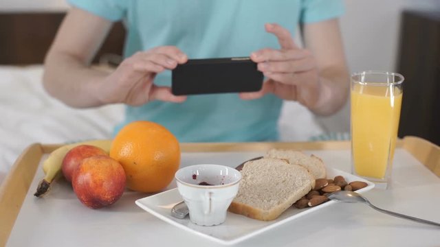 Young man sitting in bed and doing photo of his breakfast, steadycam shot
