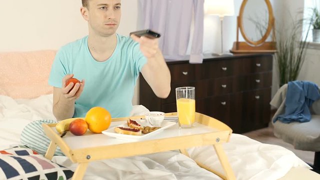 Happy boy having breakfast in bed and watching television at the morning, steadycam shot
