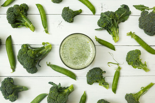 Fresh smoothies of raw broccoli and green sweet peas on a white wooden table.