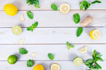 Colorful pattern of mint, lime, lemon,ginger slices. . Limes and Lemons sliced and whole with leaves. On white wooden background. Free space for text . Top view