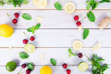 Colorful pattern of cherry, mint, lime, lemon,ginger slices. . Limes and Lemons sliced and whole with leaves. On white wooden background. Free space for text . Top view