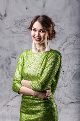 portrait of a beautiful young girl with makeup and hairstyle in a bright green dress standing with a smile looking at the dark grey background, close-up