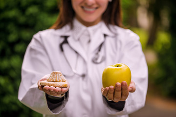 Concept junk or healthy food. Female doctor holding apple and cookie.