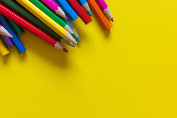 Scattered colored pencils on yellow paper background. Copy space.