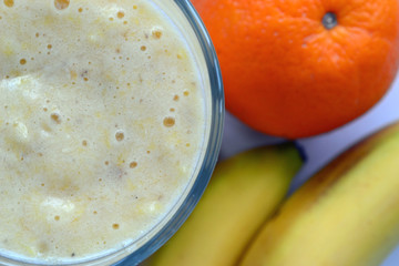 A composition of bananas and orange and a glass with smoothies
