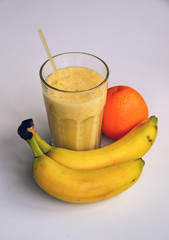 A composition of bananas and orange and a glass with smoothies