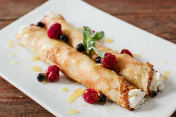 Sweet pancake with cottage cheese close up. Restaurant serving of healthy morning breakfast. Homemade rolled dessert with raspberries on white plate.