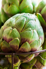 Bunch of ripe organic artichokes, green and purple color in metal basket on wood kitchen table, close up, natural light, atmospheric
