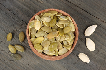 Pumpkin seeds in wooden bowl on wooden background top view with copy space