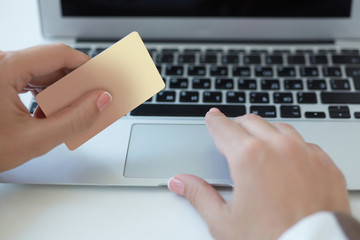 Internet banking. Close up of female hand paying bills online with laptop and credit card.Shallow depth of field with focus on the credit card.