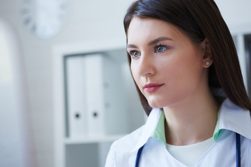 Obraz premium Beautiful female medicine doctor sitting at the table and looking at desktop computer screen.