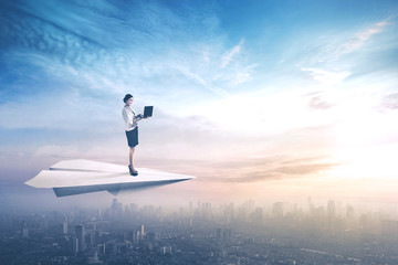 Businesswoman uses laptop on paper aeroplane